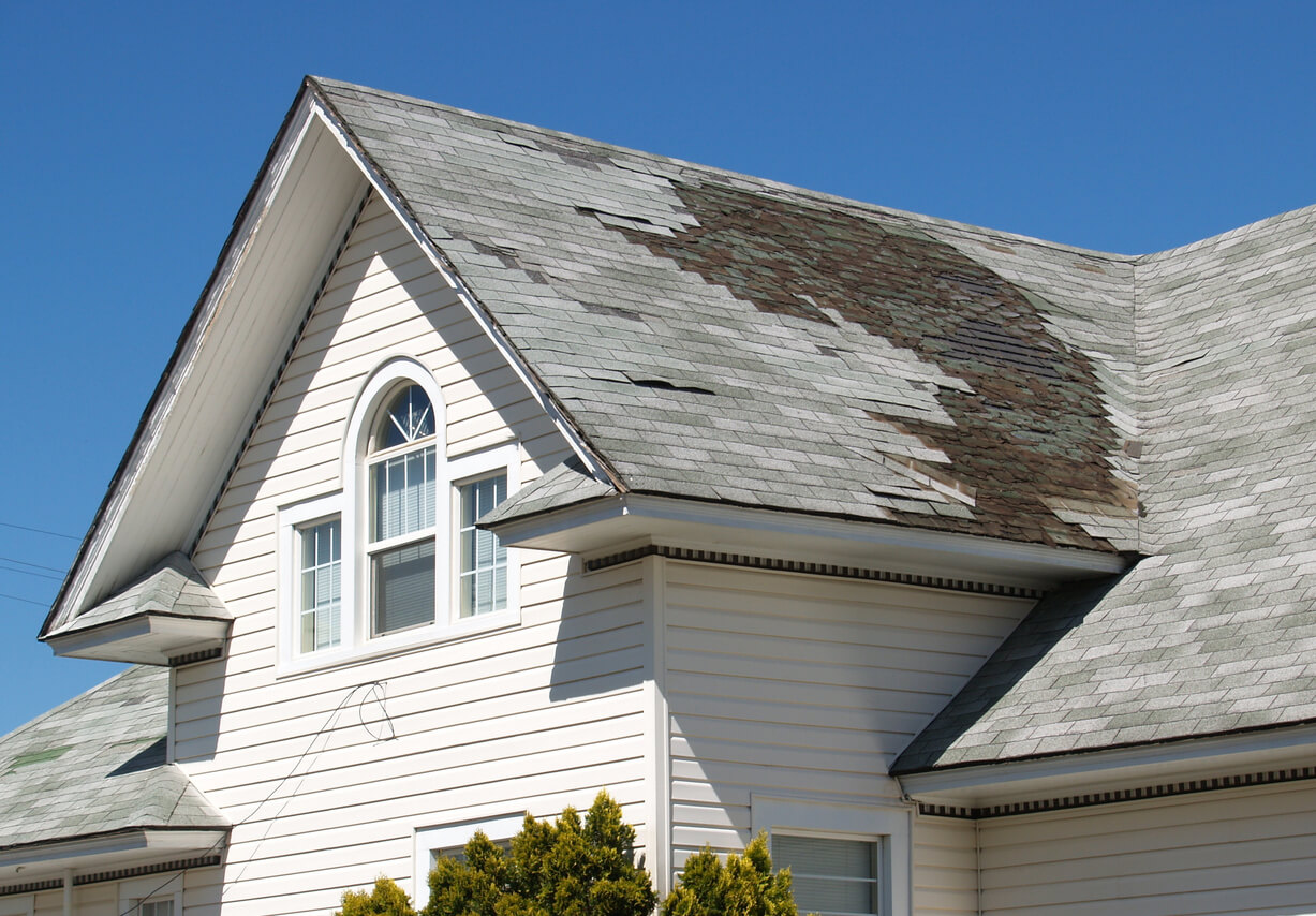 White home with damaged roof that is missing shingles